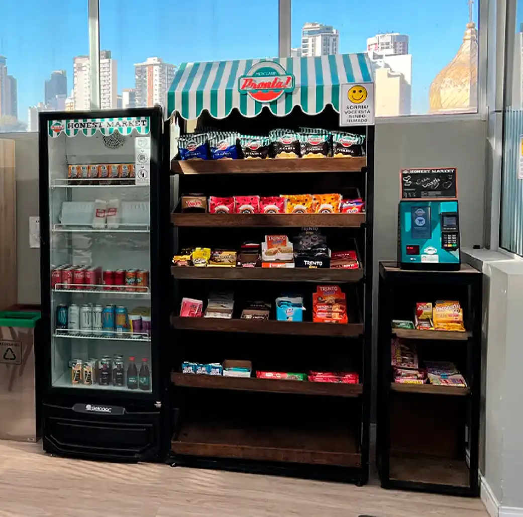 Vitrine de doces e lanches em um mercado com preferência por snacks, chocolates e bebidas, localizado em um ambiente interno com vista para prédios na cidade ao fundo.